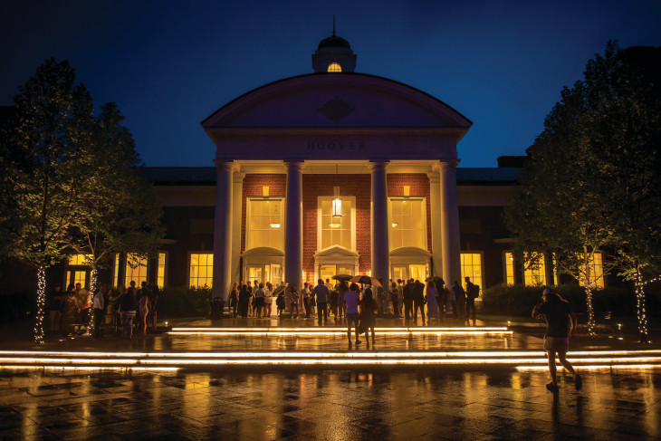 Night time on Campus with alum, students, staff, and faculty outside of a building