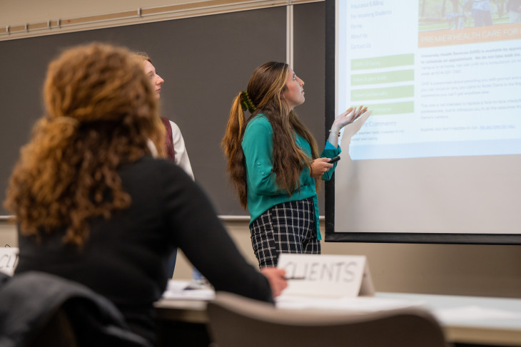 Woman presenting a PPT to a class with peers surrounding