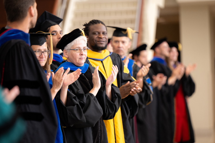 Faculty in full cap and gowns clapping 