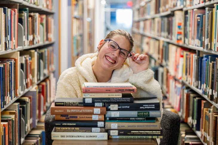 Student smiling over a stack of books in the library