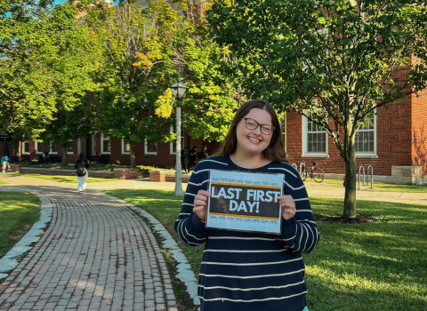 Abby stands outside with a sign that says "Last first day"